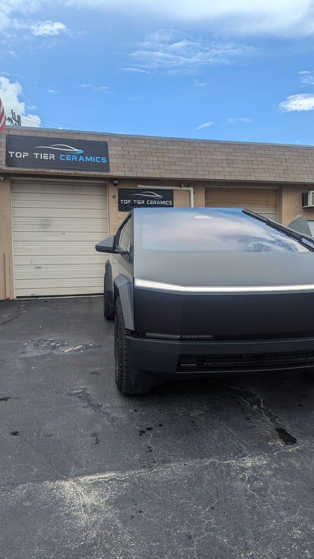 Futuristic black car parked outside Top Tier Ceramics shop under a clear sky.