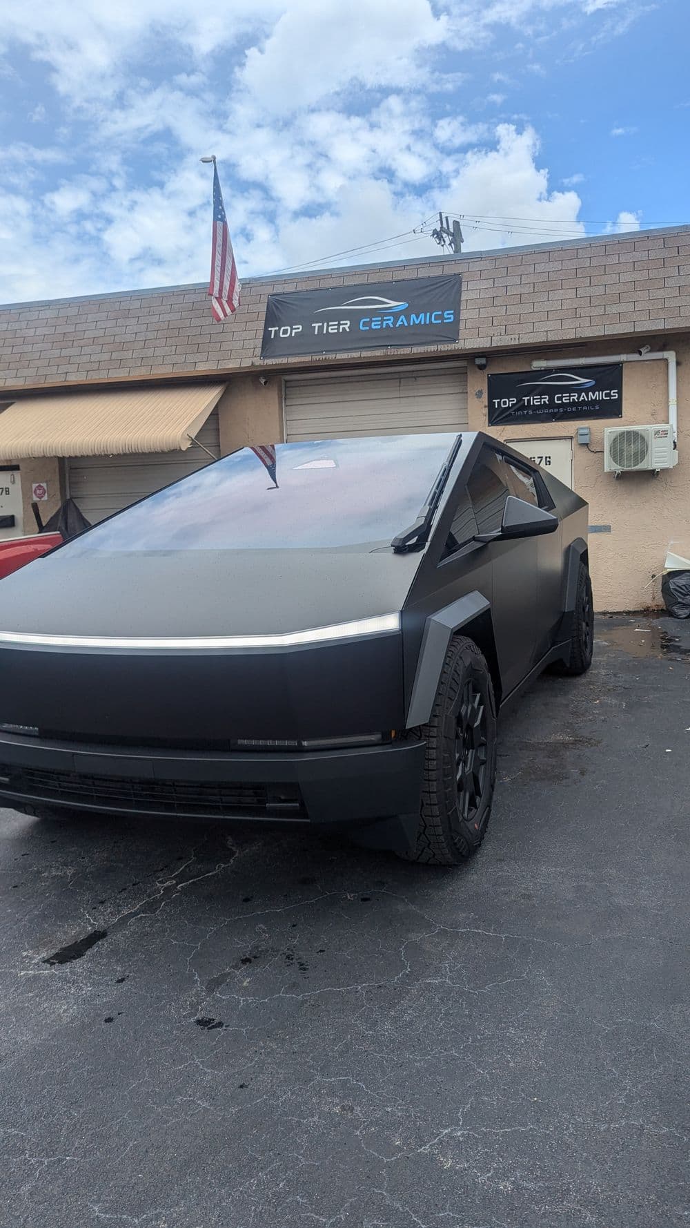 Matte black truck parked in front of Top Tier Ceramics shop, with American flag overhead.